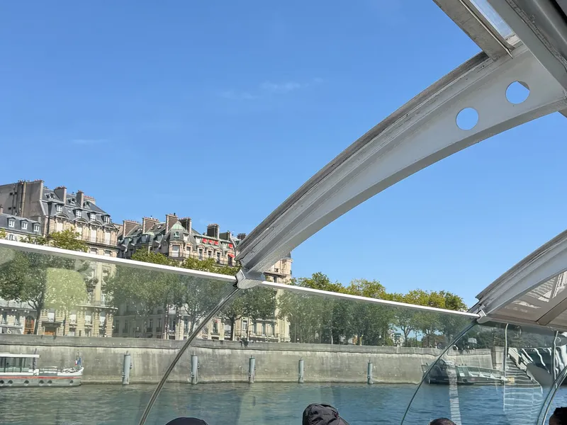 Der Blick unter einem gewölbten Glasdach eines Bootes über die Seine auf einen Kai und Wohnhäuser