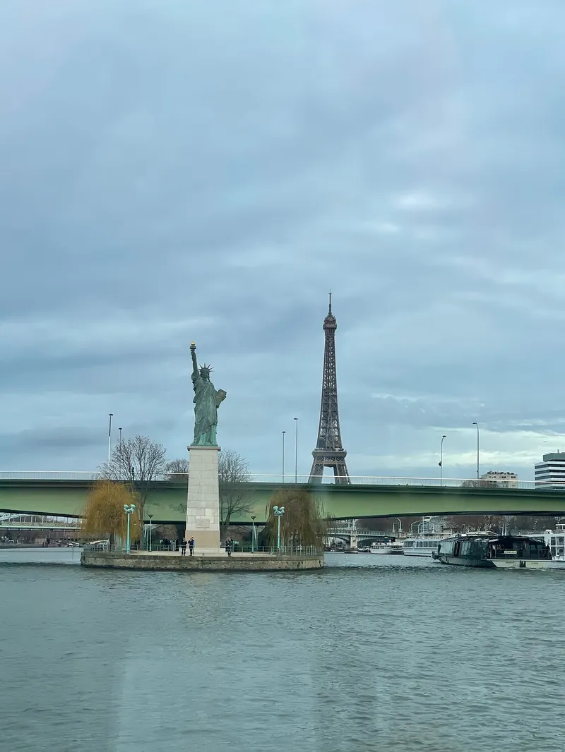 Die Nachbildung der Freiheitsstatue auf ihrer Insel in der Seine, dahinter der Eiffelturm unter grauem Himmel