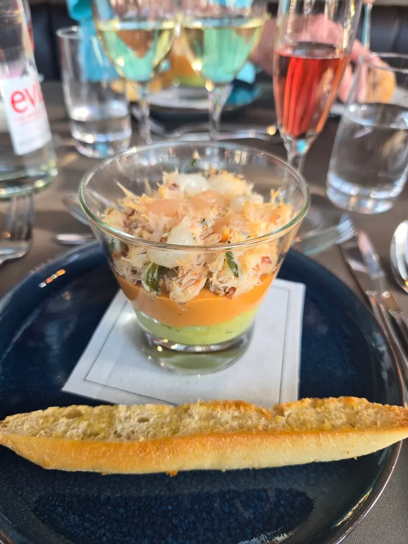 Eine geschichtete Krabbenvorspeise in einem Glas mit geröstetem Brot, dahinter Gläser mit Weißwein und Kir